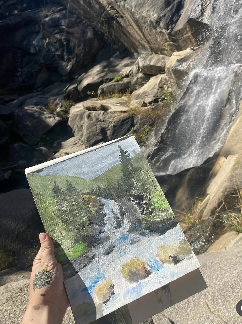 Painting of a waterfall held up outdoors near a real waterfall